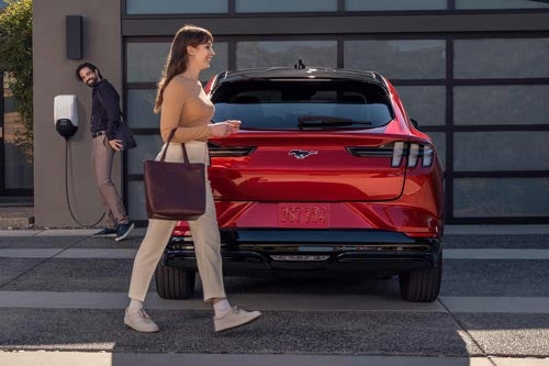 Woman walking in front of a 2024 Mustang<sup>®</sup> Mach-E charging at home